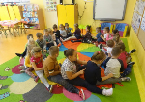 Dzieci siedzą w okręgu jeden za drugim na chuście animacyjnej wykonuje masażyk relaksacyjny.